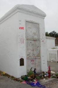Hrobka Marie Laveau v New Orleans. Její příznivci u ní dodnes nechávají zapálené svíčky a drobné dárky v podobě jídla, pití, parfémů či šperků. Opakující se motiv tří křížků je její symbolickou signaturou. Marie Laveau byla negramotná a na historických dokumentech se namísto jejího podpisu nacházejí právě tři křížky.